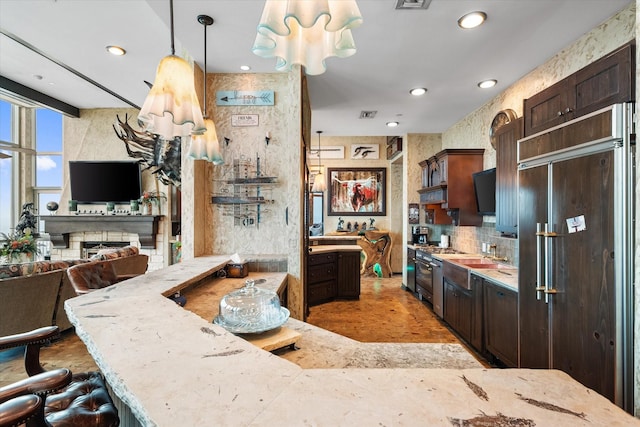 kitchen featuring a breakfast bar area, paneled built in refrigerator, hanging light fixtures, dark brown cabinets, and light stone counters