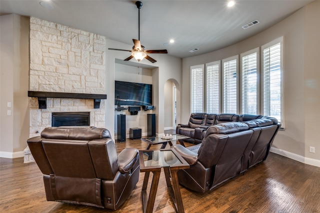 living room featuring a stone fireplace, wood-type flooring, and ceiling fan