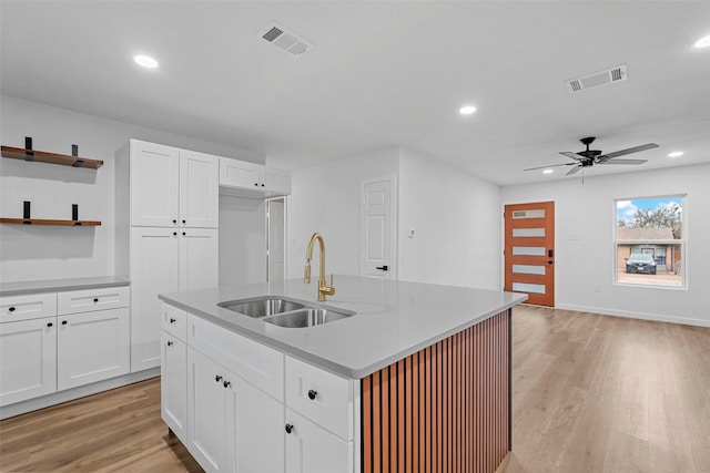 kitchen with sink, ceiling fan, white cabinetry, an island with sink, and light wood-type flooring