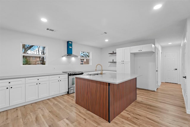 kitchen with sink, white cabinetry, a center island with sink, stainless steel electric range, and wall chimney range hood