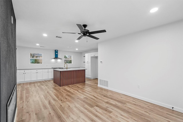 kitchen with white cabinetry, an island with sink, light hardwood / wood-style floors, and wall chimney exhaust hood