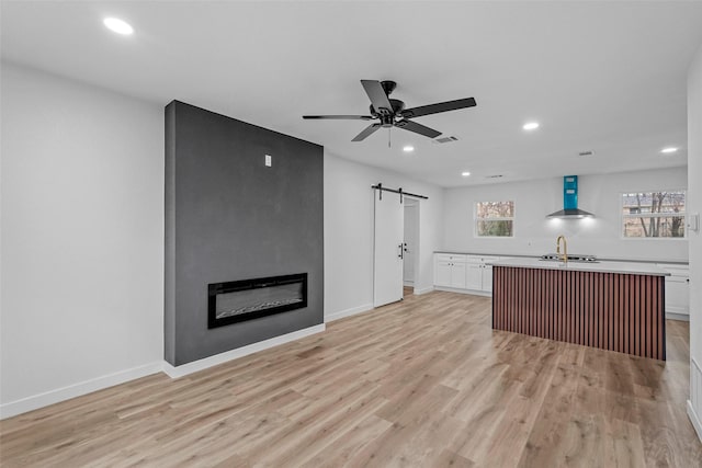 unfurnished living room featuring ceiling fan, a large fireplace, a barn door, and light hardwood / wood-style flooring