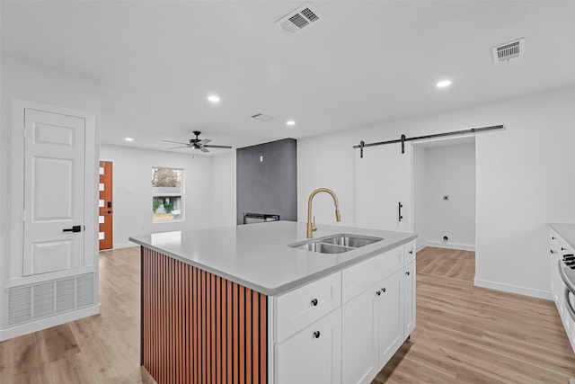 kitchen with sink, an island with sink, white cabinets, a barn door, and light wood-type flooring