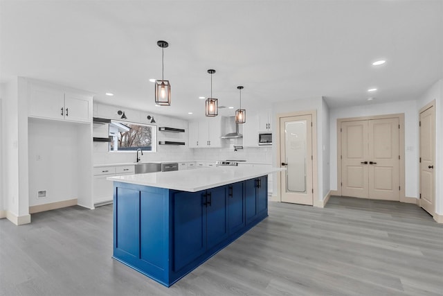 kitchen with white cabinets, a center island, built in microwave, light countertops, and wall chimney range hood