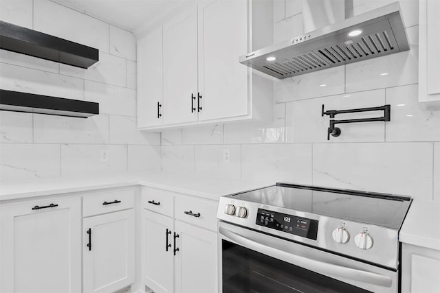 kitchen with stainless steel electric range oven, decorative backsplash, white cabinetry, wall chimney range hood, and light stone countertops