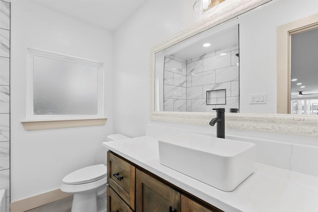 full bath featuring toilet, baseboards, tiled shower, and vanity