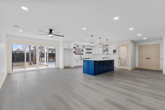 kitchen featuring a kitchen island, white cabinetry, light countertops, wall chimney range hood, and open shelves