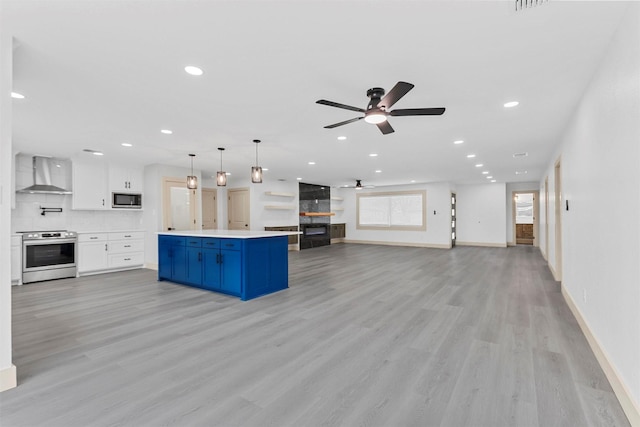 kitchen featuring stainless steel appliances, light countertops, open floor plan, white cabinets, and wall chimney exhaust hood