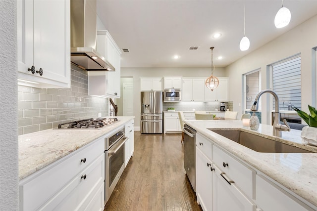 kitchen with stainless steel appliances, white cabinetry, decorative light fixtures, and wall chimney exhaust hood