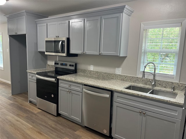 kitchen featuring sink, appliances with stainless steel finishes, gray cabinetry, wood-type flooring, and light stone countertops