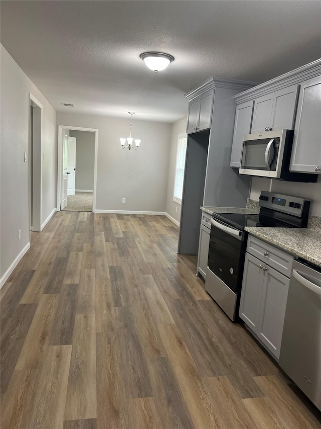 kitchen featuring gray cabinets, appliances with stainless steel finishes, hardwood / wood-style floors, and a notable chandelier