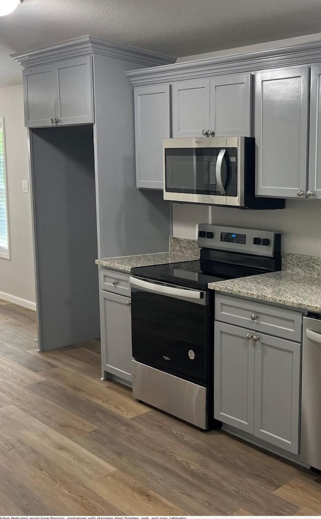 kitchen with light hardwood / wood-style flooring, gray cabinets, a textured ceiling, and appliances with stainless steel finishes