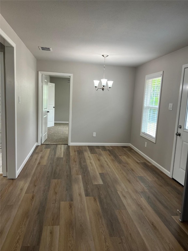 unfurnished dining area with dark wood-type flooring, a textured ceiling, and a chandelier