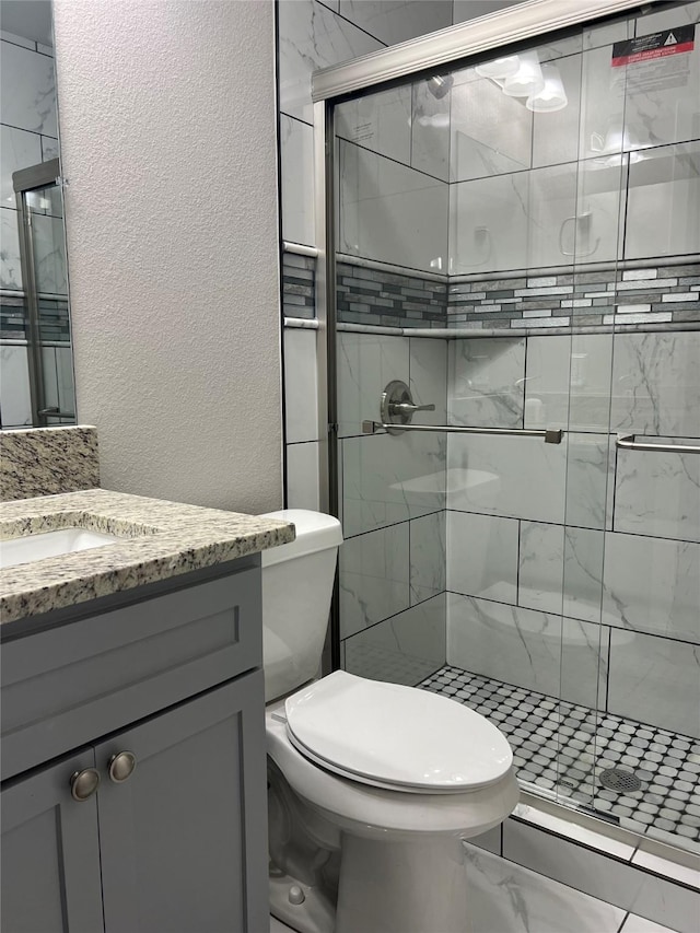 bathroom featuring vanity, a shower with shower door, and toilet