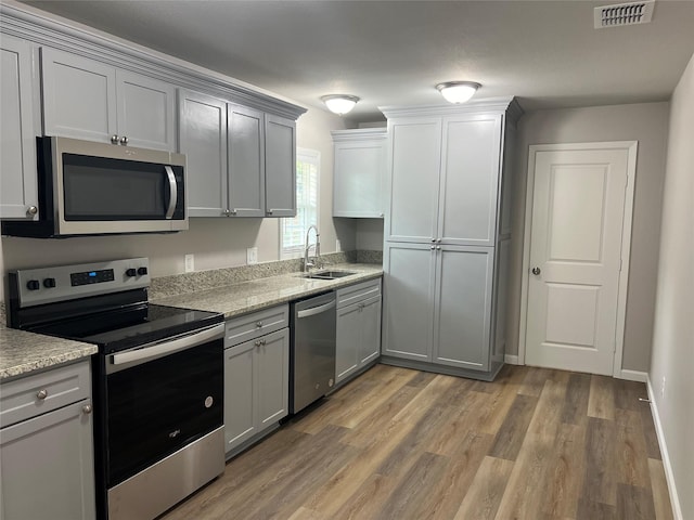 kitchen with gray cabinetry, sink, stainless steel appliances, and light hardwood / wood-style floors