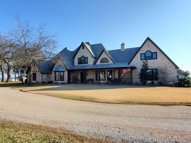 french country home featuring metal roof, stone siding, a front lawn, a standing seam roof, and a chimney