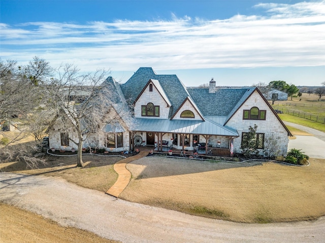 french country home with metal roof, dirt driveway, stone siding, a front lawn, and a standing seam roof