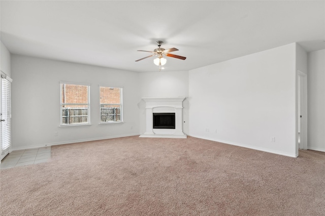 unfurnished living room with light carpet, a fireplace with raised hearth, ceiling fan, and baseboards