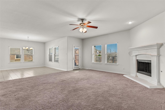 unfurnished living room featuring carpet, a healthy amount of sunlight, a fireplace with raised hearth, and ceiling fan with notable chandelier