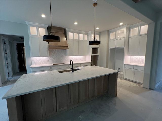 kitchen with sink, decorative light fixtures, a center island with sink, light stone countertops, and white cabinets