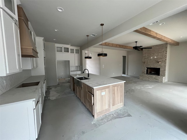 kitchen featuring pendant lighting, sink, white cabinets, a center island with sink, and cooktop