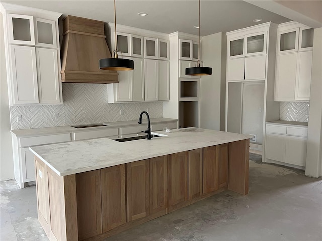 kitchen with hanging light fixtures, custom range hood, a center island with sink, and black stovetop