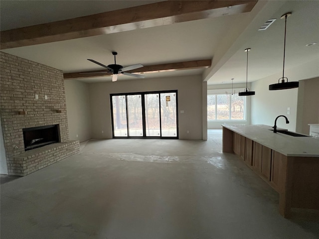 unfurnished living room with ceiling fan, a fireplace, beam ceiling, and sink