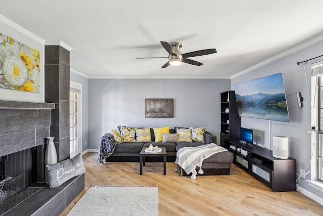 living room featuring ceiling fan, ornamental molding, a fireplace, and light hardwood / wood-style flooring