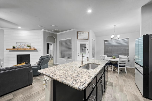 kitchen featuring pendant lighting, sink, a fireplace, light stone countertops, and an island with sink