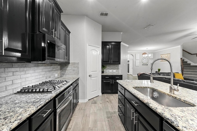 kitchen with sink, backsplash, stainless steel appliances, light stone countertops, and light wood-type flooring