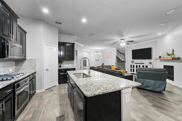 kitchen featuring a fireplace, sink, stainless steel appliances, a center island with sink, and light wood-type flooring