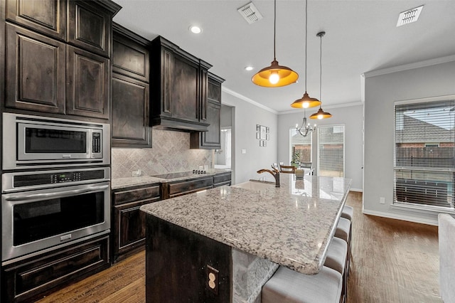 kitchen featuring appliances with stainless steel finishes, a breakfast bar area, hanging light fixtures, light stone counters, and a center island with sink