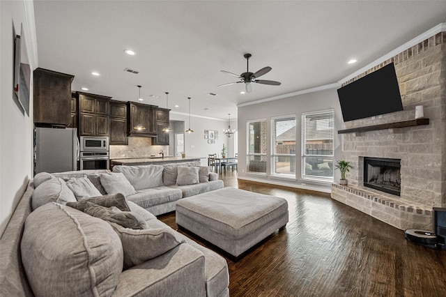 living room with crown molding, dark hardwood / wood-style flooring, ceiling fan with notable chandelier, and a stone fireplace