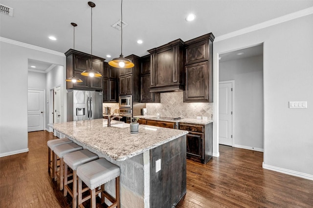 kitchen featuring appliances with stainless steel finishes, decorative light fixtures, an island with sink, backsplash, and light stone counters