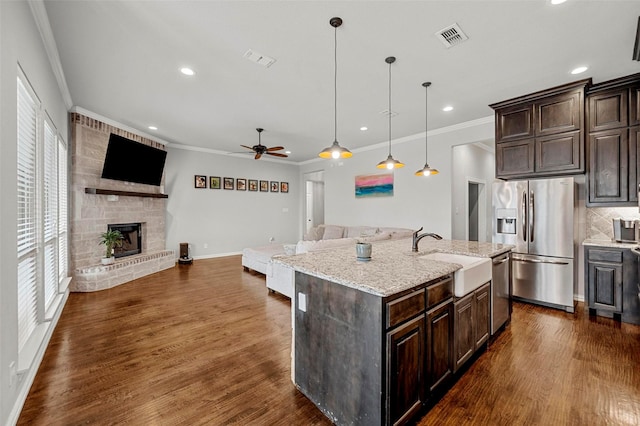 kitchen featuring a stone fireplace, pendant lighting, an island with sink, sink, and stainless steel appliances