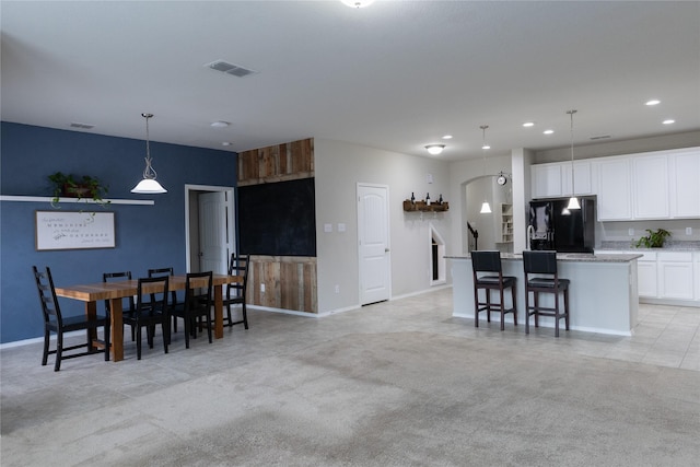 kitchen featuring a breakfast bar, black fridge with ice dispenser, a center island, hanging light fixtures, and white cabinets