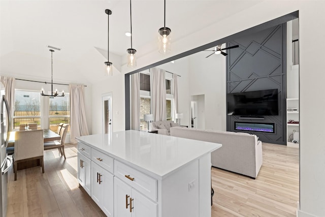 kitchen featuring lofted ceiling, decorative light fixtures, a center island, light hardwood / wood-style floors, and white cabinets