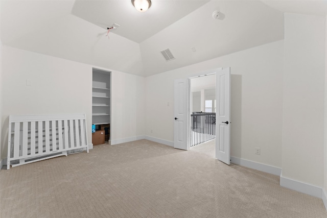 carpeted empty room with lofted ceiling and built in shelves