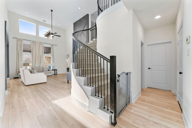 stairway with ceiling fan, wood-type flooring, and a high ceiling