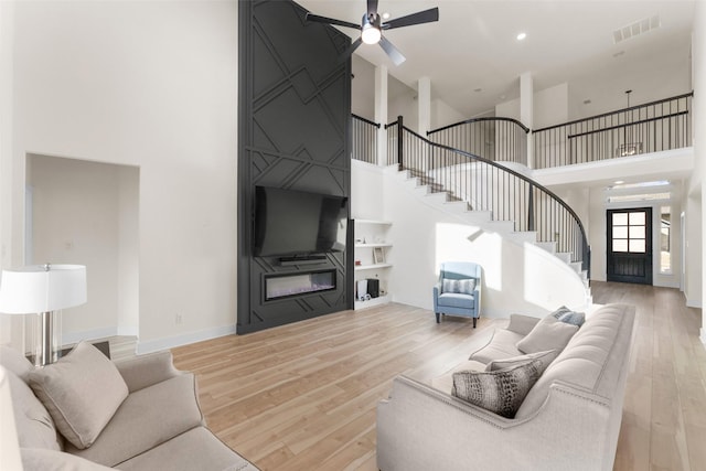 living room featuring ceiling fan, a towering ceiling, a fireplace, and light wood-type flooring