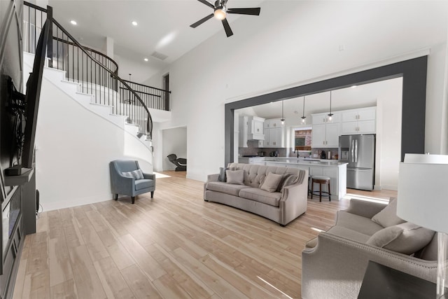 living room featuring ceiling fan, light hardwood / wood-style flooring, and a towering ceiling