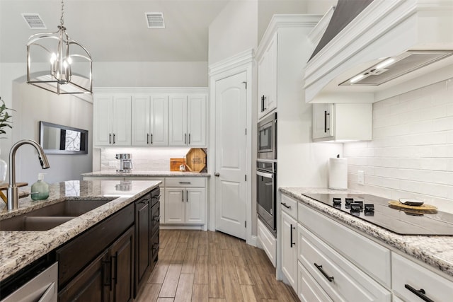 kitchen featuring light stone counters, stainless steel appliances, premium range hood, white cabinetry, and a sink