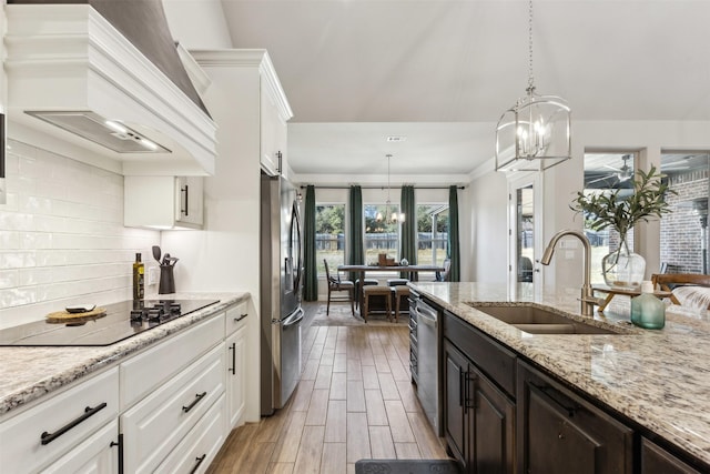 kitchen featuring custom exhaust hood, stainless steel appliances, an inviting chandelier, white cabinetry, and a sink