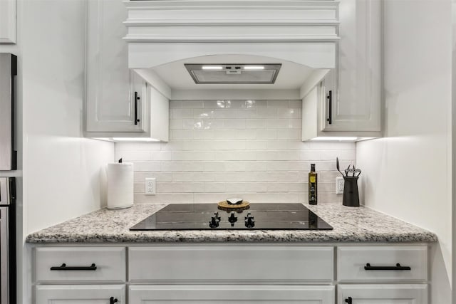 kitchen with black electric stovetop, light stone countertops, premium range hood, white cabinets, and decorative backsplash