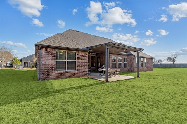 rear view of property with roof with shingles, brick siding, a lawn, and a patio