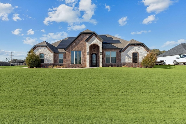 french country home featuring a front yard, brick siding, roof with shingles, and solar panels