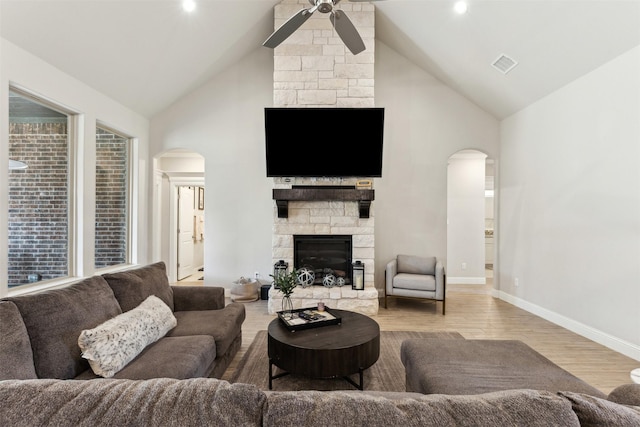 living room featuring arched walkways, visible vents, ceiling fan, a stone fireplace, and wood finished floors