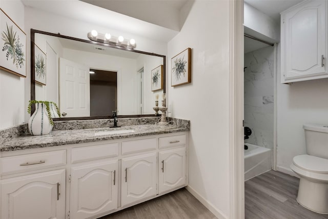 full bathroom with hardwood / wood-style flooring, tiled shower / bath, vanity, and toilet