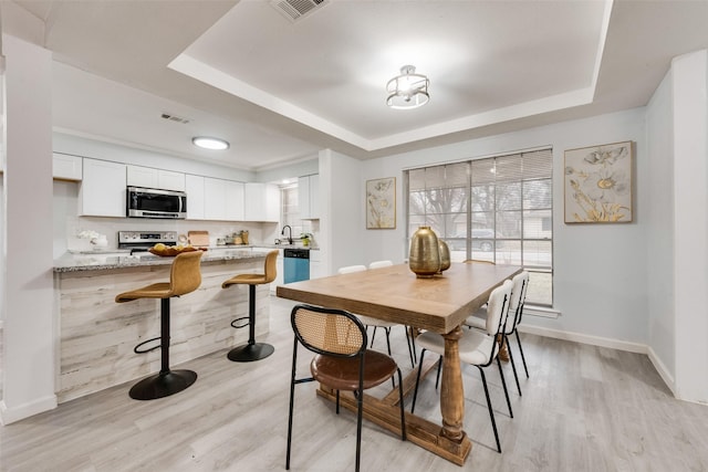 dining area featuring a tray ceiling, sink, and light wood-type flooring