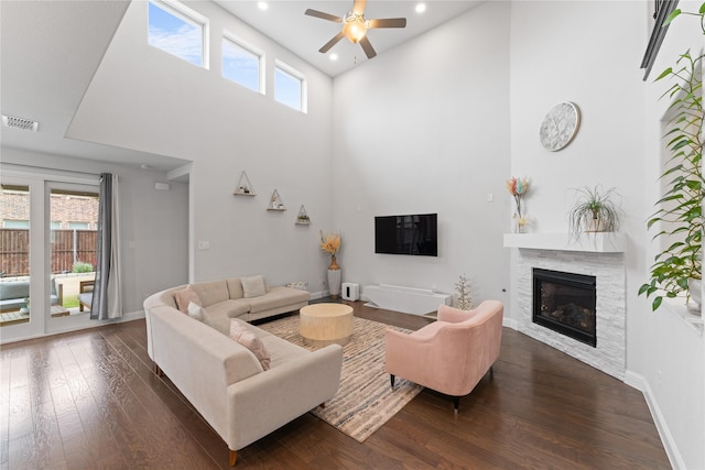 living room with visible vents, dark wood finished floors, a towering ceiling, and a tiled fireplace